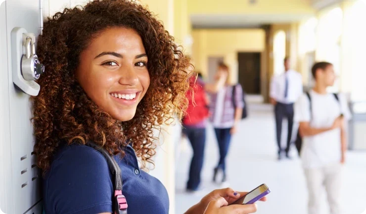 Teen girl leaning on lockers in school hallway while holding phone