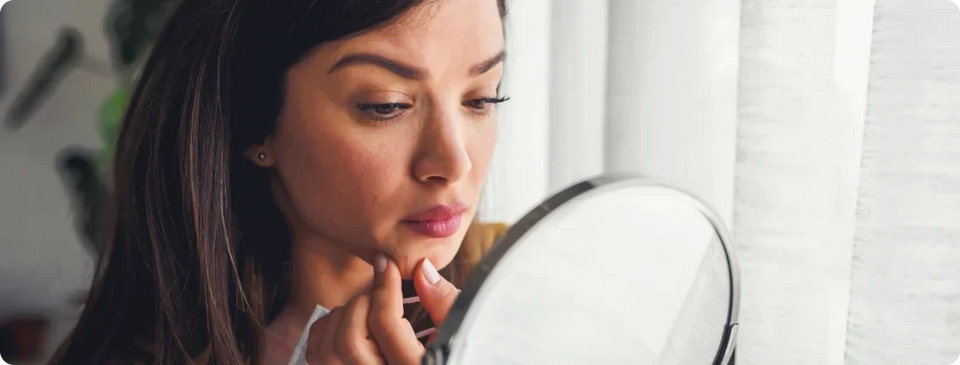 woman touching her chin and looking into mirror