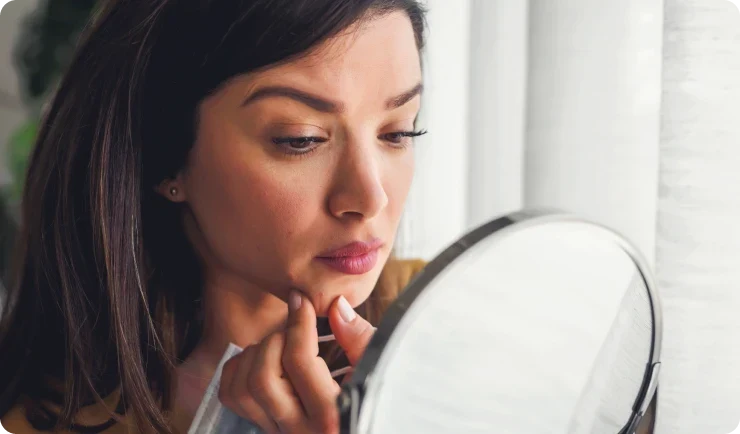 woman looking into mirror and touching chin